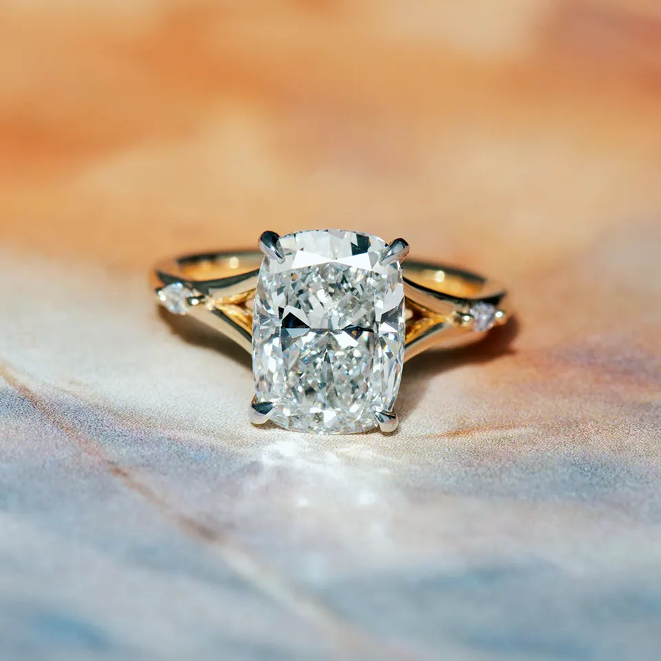 Elongated cushion-cut diamond in white claws on a yellow gold split-shank band set with a small diamond on each side