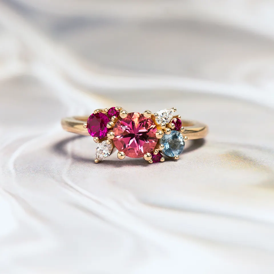 Yellow gold cluster ring: a round pink centre stone among smaller magenta and pale blue stones and two pear-cut diamonds