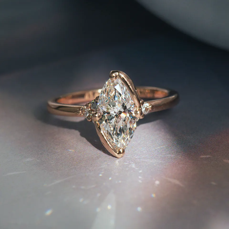 Marquise diamond set on the diagonal in a rose gold half-bezel, with small round diamonds at each shoulder