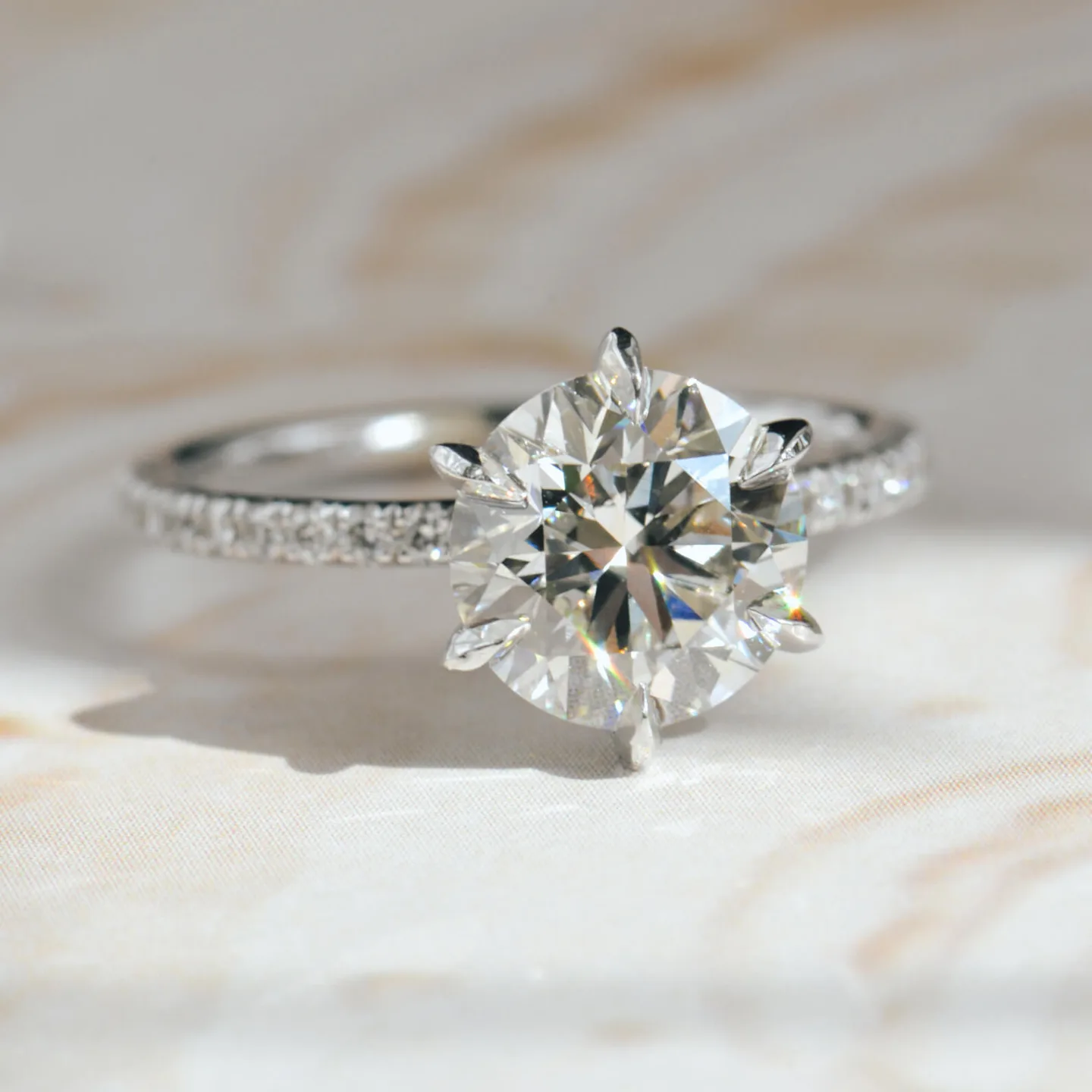 Round pavé engagement ring: a round brilliant diamond in six claw prongs on a white metal pavé band